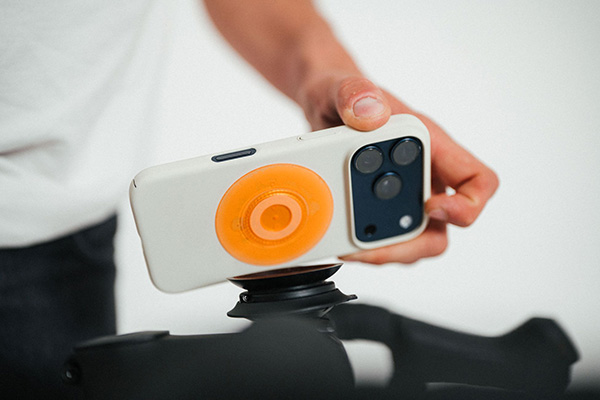 FIDLOCK - VACUUM uni phone patch - Smartphone mit organen Patch wird an Base gehalten - kompr.